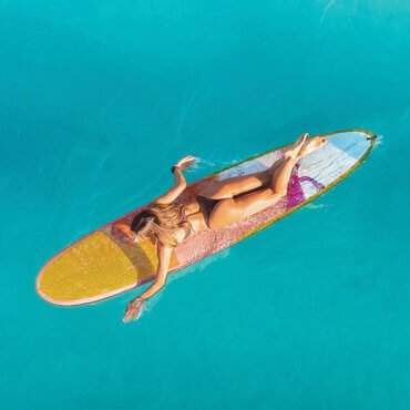 Photo of girl with yellow surfboard swimming out into the clear blue ocean.