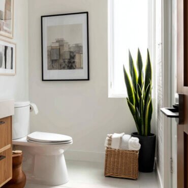 Neutral bathroom featuring framed abstract wall art above the toilet, wood vanity, wicker basket, and tall green plant