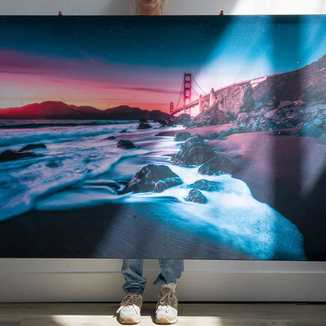 Colorful nature photo printed as large custom wall art being held by girl in living room with white walls.