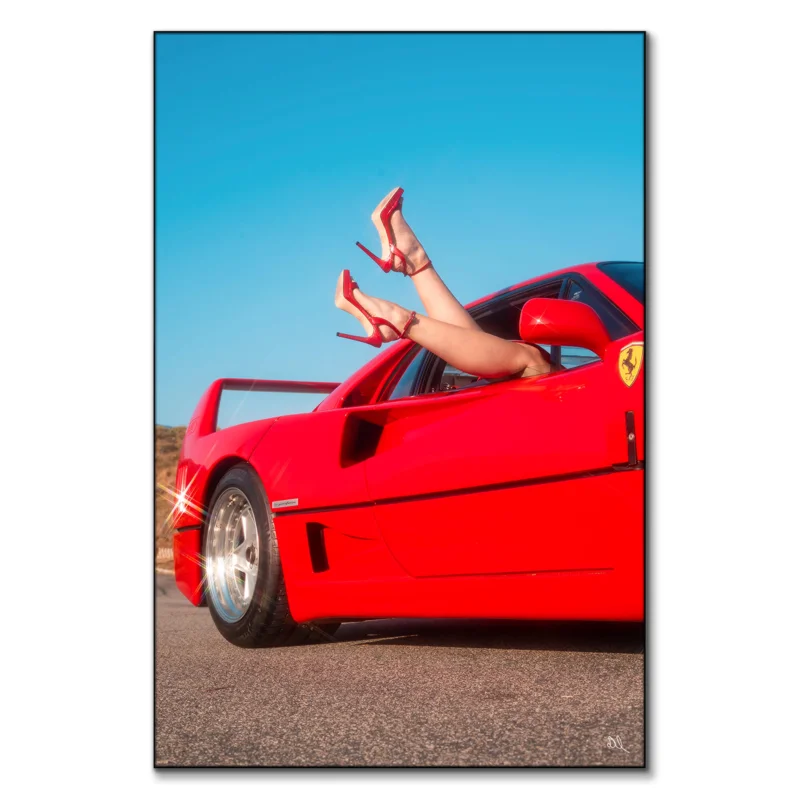 Red sports car with legs in red high heels playfully extending from the window under a blue sky.