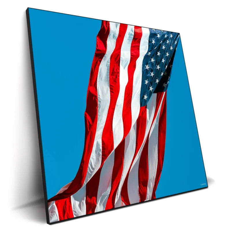 Photograph of the American flag waving in the wind against a clear blue sky.