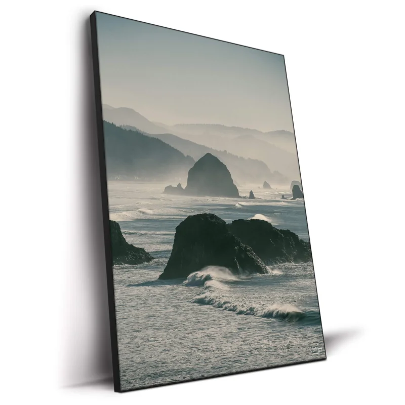 A misty coastal landscape featuring rugged sea stacks emerging from ocean waves, with rolling hills in the background.